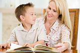 Woman and young boy reading book in dining room smiling