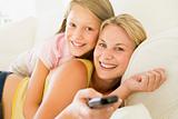 Woman and young girl with remote control embracing on sofa smili