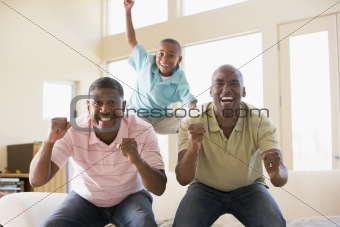 Two men and young boy in living room cheering and smiling