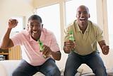 Two men in living room with beer bottles cheering and smiling