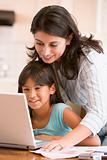Woman and young girl in kitchen with laptop and paperwork smilin