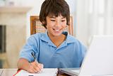 Young boy with laptop doing homework in dining room smiling