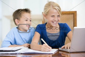 Two young children with laptop doing homework in dining room smi