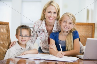 Woman helping two young children with laptop do homework in dini