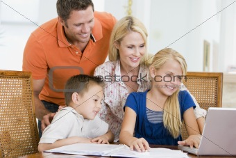 Couple helping two young children with laptop do homework in din