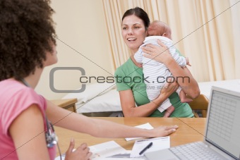 Doctor with laptop and woman in doctor's office holding baby