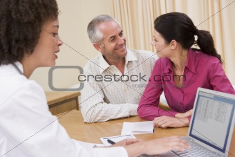 Doctor with laptop and couple in doctor's office smiling