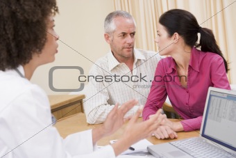 Doctor with laptop and couple in doctor's office frowning