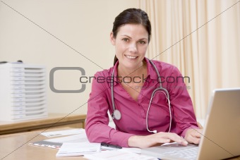 Doctor using laptop in doctor\'s office smiling