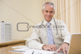Doctor using laptop in doctor's office smiling