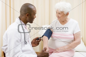 Doctor checking woman's blood pressure in exam room smiling