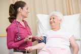 Doctor checking woman's blood pressure in exam room smiling