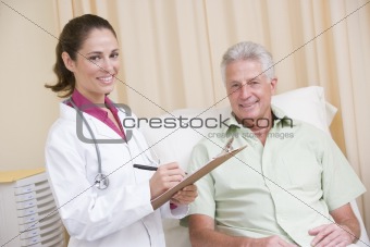 Doctor writing on clipboard while giving checkup to man in exam 