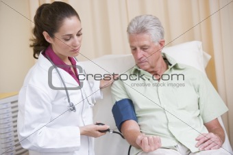 Doctor checking man's blood pressure in exam room