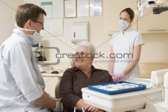 Dentist and assistant in exam room with woman in chair smiling