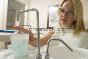 Woman in dental exam room reaching for water