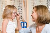 Woman trying eyeglasses on young girl at optometrists smiling