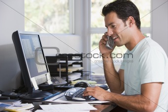 Man in home office on telephone using computer and smiling