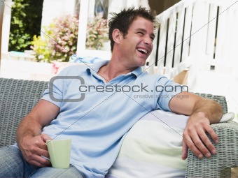 Man sitting on patio with coffee laughing