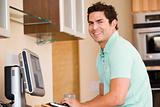 Man in kitchen using computer and smiling