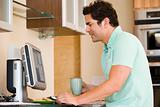 Man in kitchen with coffee using computer and smiling