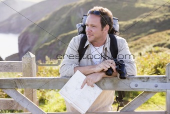 Man relaxing on cliffside path holding map and binoculars