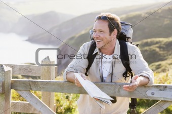 Man relaxing on cliffside path holding map and laughing