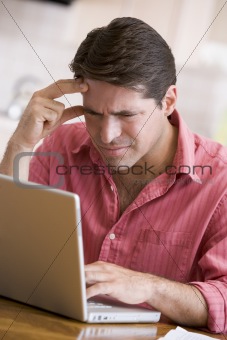Man in kitchen using laptop frowning
