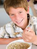 Young boy in kitchen eating soup and smiling
