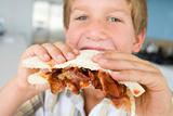 Young boy in kitchen eating bacon sandwich
