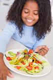 Young girl in kitchen eating salad smiling