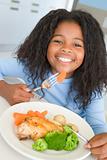 Young girl in kitchen eating chicken and vegetables smiling