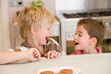 Two young boys in kitchen eating cookies smiling