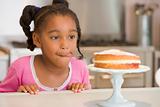 Young girl in kitchen looking at cake on counter