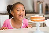 Young girl in kitchen looking at cake on counter smiling
