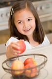 Young girl in kitchen getting apple off counter smiling