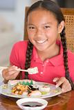 Young girl in dining room eating Chinese food smiling