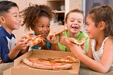 Four young children indoors eating pizza smiling