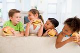 Four young children eating cheeseburgers in living room smiling