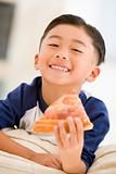 Young boy eating pizza slice in living room smiling