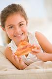 Young girl eating pizza slice in living room smiling