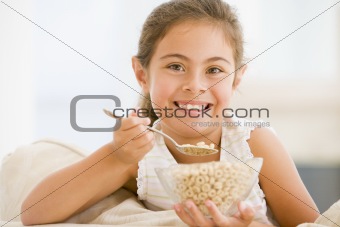 Young girl eating cereal in living room smiling