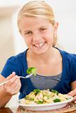 Young girl indoors eating pasta with brocolli smiling