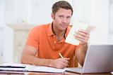 Man in dining room with laptop holding paperwork