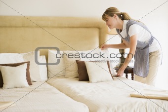 Maid making bed in hotel room smiling