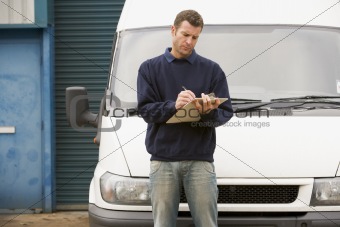 Deliveryperson standing with van writing in clipboard