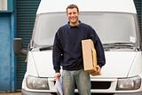 Deliveryperson standing with van holding clipboard and box smili