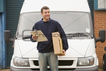 Deliveryperson standing with van holding clipboard and box smili