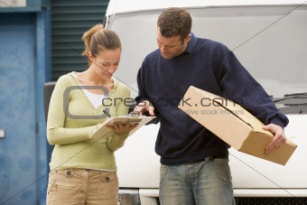 Two deliverypeople standing with van holding clipboard and box