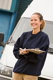 Deliveryperson standing with van writing in clipboard smiling